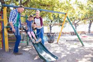 Happy parents looking at daughter playing on slide