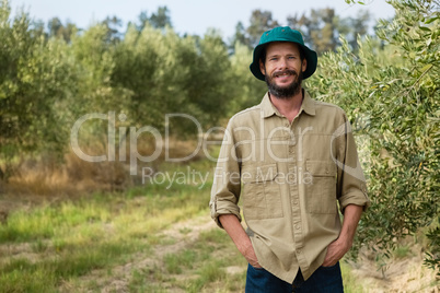 Smiling farmer standing with hands in pocket in olive farm