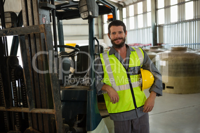 Smiling worker leaning on forklift in factory
