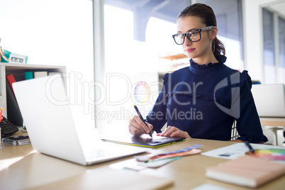 Female executive working over laptop and graphic tablet at her desk