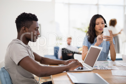 Male executive working on laptop while female executive using mobile phone at desk