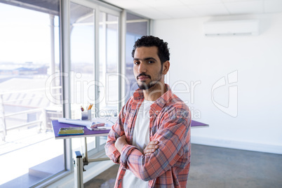 Male architect standing with arms crossed in office