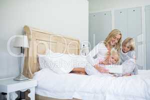 Mother and kids using digital tablet on bed in bed room