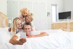 Happy family taking a selfie on mobile phone in the bed room