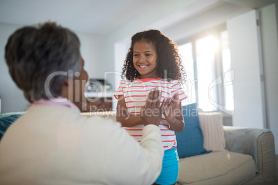 Granddaughter and grandmother playing clapping games on sofa in living room