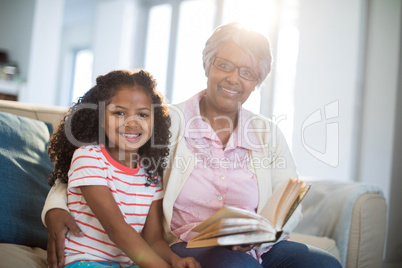 Smiling grandmother and daughter reading book in living room