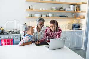 Happy family using graphic tablet while looking at laptop in kitchen