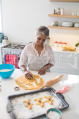 Smiling senior woman preparing cookies in kitchen