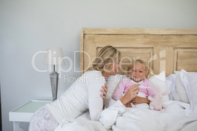 Mother checking sick daughter temperature with digital thermometer in the bedroom