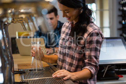 Barmaid preparing drink with customer in background