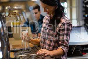 Barmaid preparing drink with customer in background