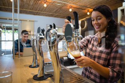 Young barmaid pouring beer from tap in glass