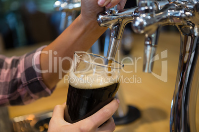 Cropped hands of barmaid pouring drink from tap in glass
