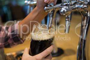 Cropped hands of barmaid pouring drink from tap in glass