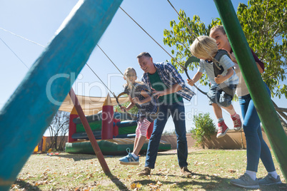 Playful parents swinging children at playground