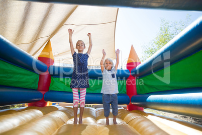 Portrait of happy siblings with arms raised jumping on bouncy castle