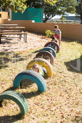 Children playing by tyres at playground during sunny day