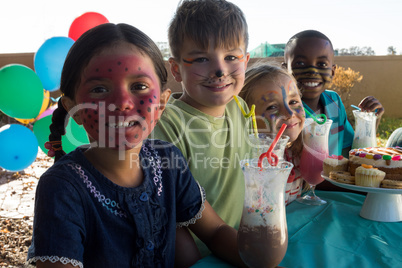 Smiling children with face paint sitting by food and drinks at park