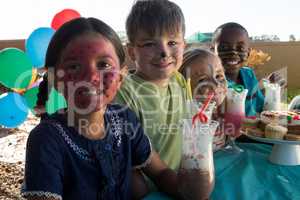 Smiling children with face paint sitting by food and drinks at park