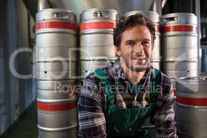 Smiling male worker sitting by kegs at warehouse