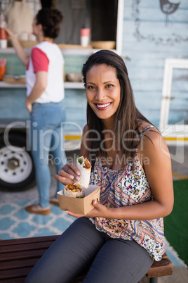 Woman sitting on bench and eating wrap