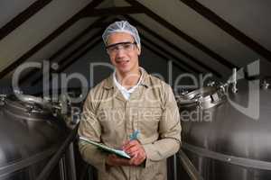 Portrait of worker amidst storage tanks writing on clipboard