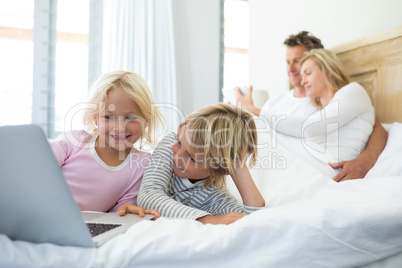 Family using digital tablet and laptop on bed in the bed room