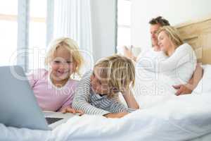 Family using digital tablet and laptop on bed in the bed room