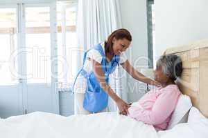 Female doctor comforting senior woman on bed