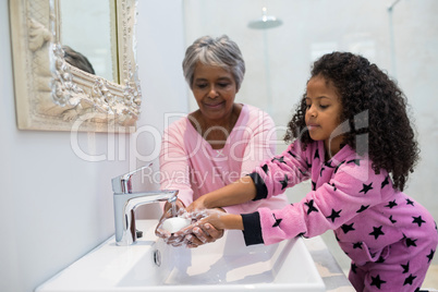 Grandmother and granddaughter washing hands with soap in bathroom sink