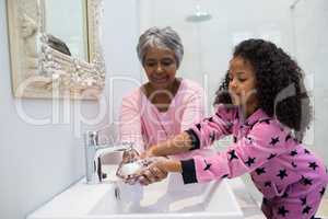 Grandmother and granddaughter washing hands with soap in bathroom sink
