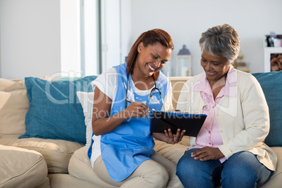 Doctor explaining medication on clipboard to senior woman in living room