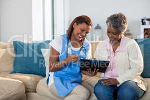 Doctor explaining medication on clipboard to senior woman in living room