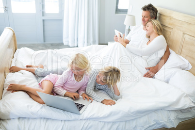 Family using digital tablet and laptop on bed in the bed room