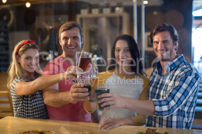 Portrait of happy friends toasting beer at table in bar