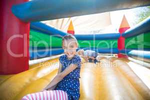 Happy girl sitting on bouncy castle while brother playing in background