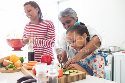 Grandmother assisting granddaughter to chop vegetables in kitchen