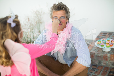 Cute daughter in fairy costume putting makeup on her fathers face