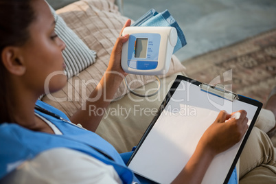 Doctor holding blood pressure monitor and writing on clipboard