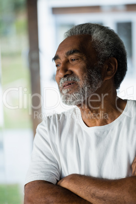 Senior man standing with arms crossed at home