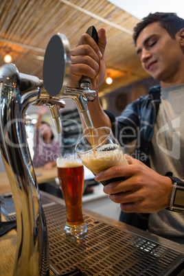 Young bartender pouring drink from tap in glass