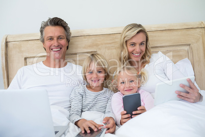 Family using digital tablet, mobile phone and laptop on bed in the bed room