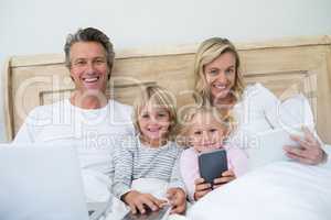 Family using digital tablet, mobile phone and laptop on bed in the bed room