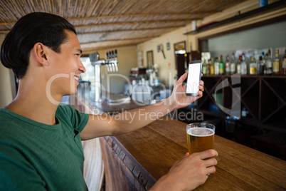 Smiling man taking selfie while having beer at bar