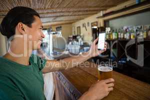 Smiling man taking selfie while having beer at bar