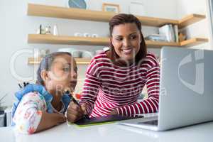 Mother and daughter using graphic tablet while looking at laptop