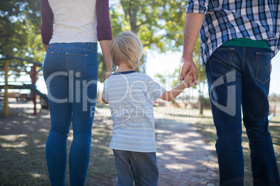 Parents and boy holding hands while walking on footpath at park