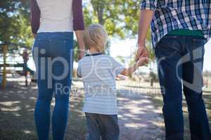 Parents and boy holding hands while walking on footpath at park