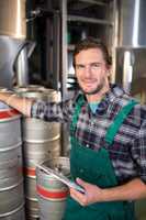 Smiling worker holding clipboard while standing by kegs at warehouse