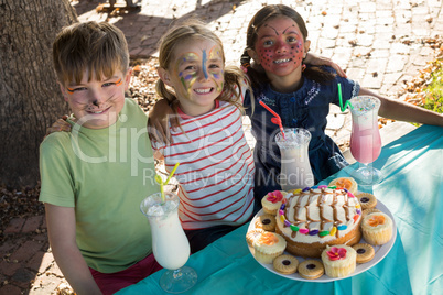 Happy friends with face paint sitting by food and drink at table